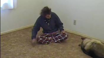 Long-haired man aggressively bangs his well-trained dog on the rug